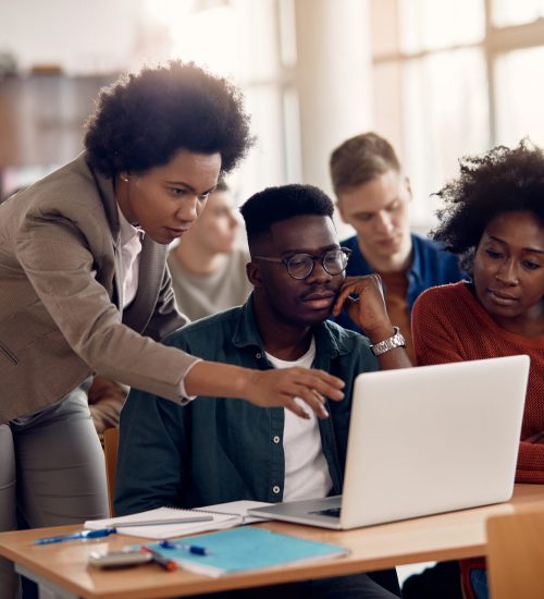 African American professor and her students using laptop during lecture in the classroom.